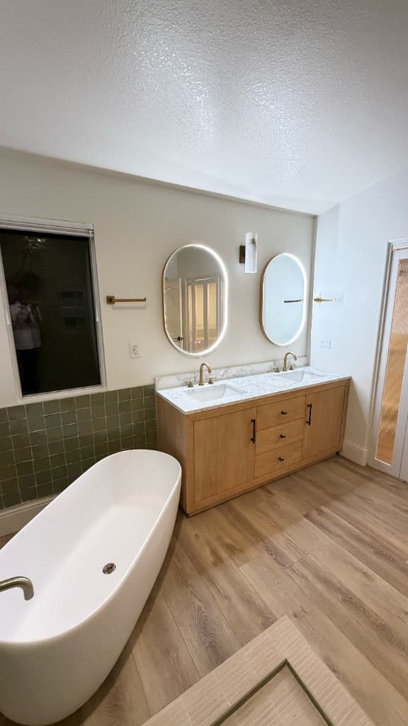 Primary bathroom remodel in Carlsbad with a freestanding tub, oak double vanity, and sage tile