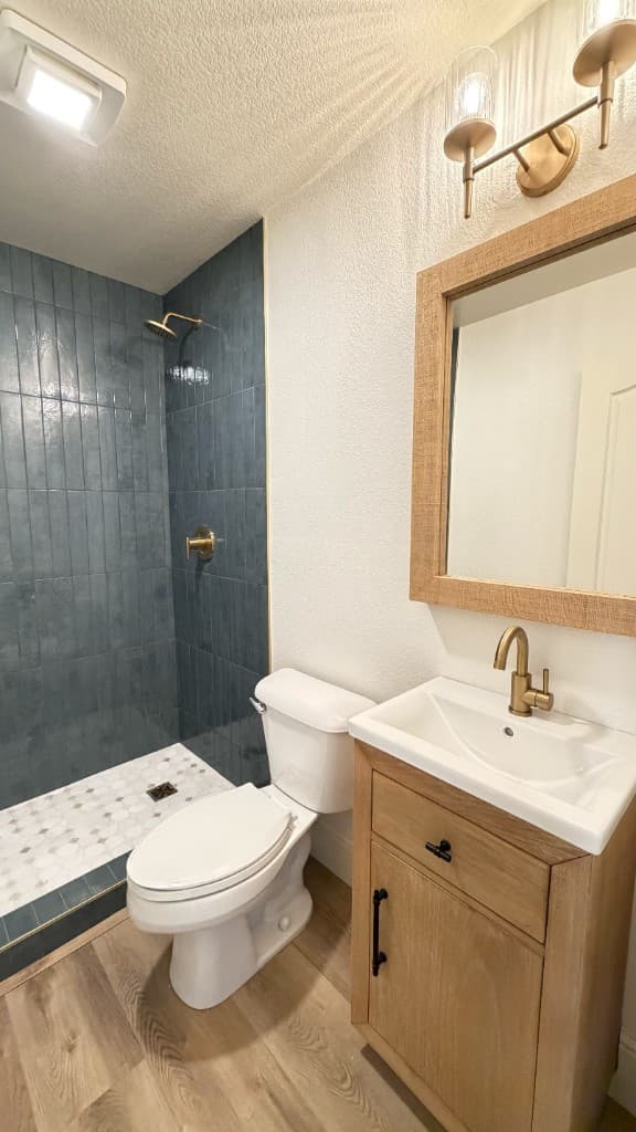 Oak vanity, brass faucet, and blue-gray shower in a Carlsbad guest bathroom