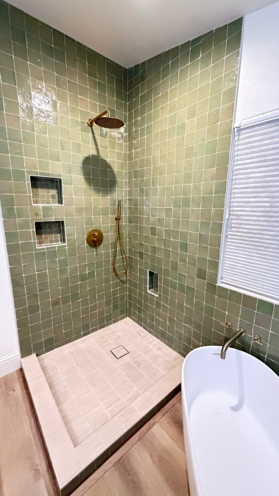 Sage green tiled walk-in shower with brass fixtures in a Carlsbad primary bath